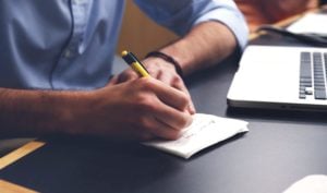 Man writing list by laptop computer