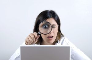 Woman with magnifying glass looking at laptop screen